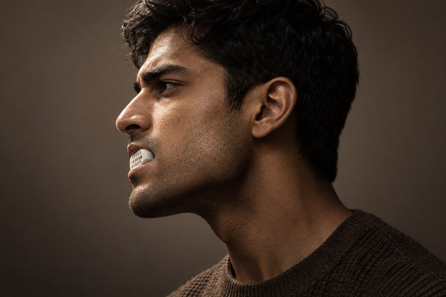 Man in profile biting down on a white Grit jaw trainer